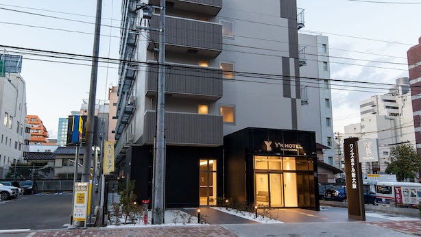 A modern hotel building with multiple floors, a prominent sign, and a well-lit entrance. - Y’s Hotel Shin - Osaka (Osaka)
