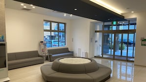A modern lobby with a central seating area, large windows, and a glass door entrance. - Y’s Hotel Shin - Osaka (Osaka)