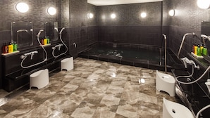 A modern bathroom with dark tiled walls, a large bathtub, and two sinks with mirrors. - Y’s Hotel Shin - Osaka (Osaka)
