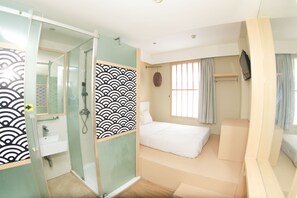 Una habitación de hotel moderna con cabina de ducha de vidrio, cama con colchón blanco y televisor montado en la pared.