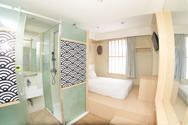 A modern hotel room with a glass shower enclosure, a bed with a white mattress, and a television mounted on the wall. - Kimono Hotel (Kuta)