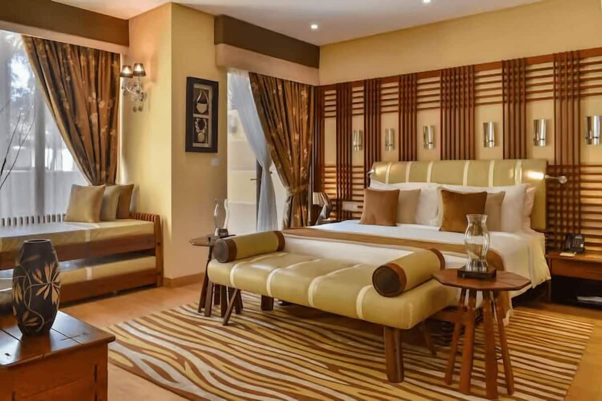A modern hotel room with a large bed, a sofa, a small table, and a decorative vase.