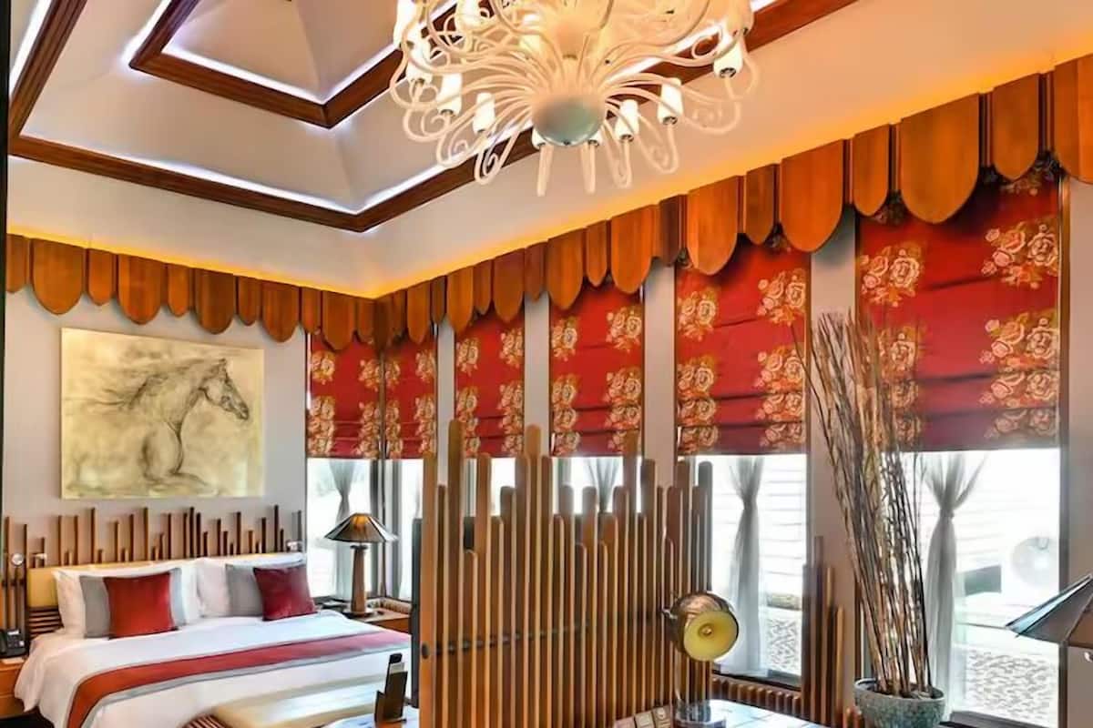 A hotel room with a bed, a desk, a chair, a lamp, and a large window with curtains.