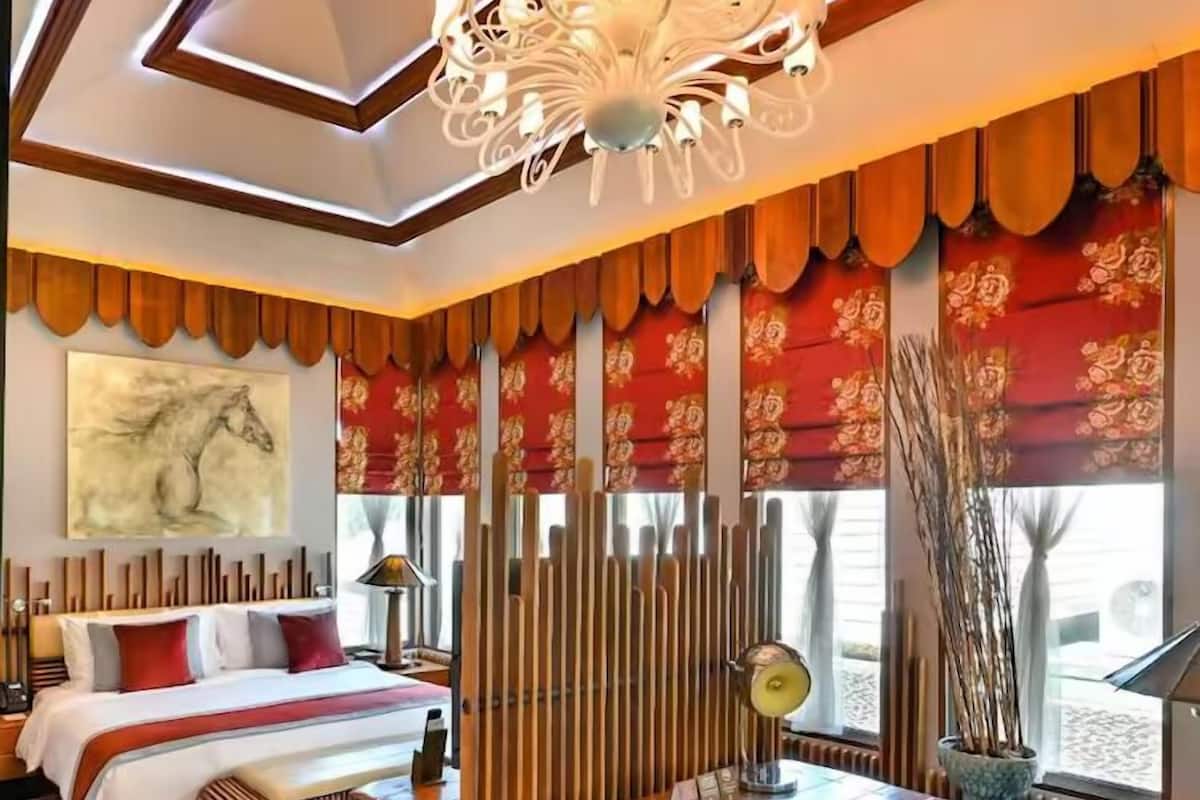 A modern hotel room with a bed, a desk, a chair, a lamp, and a large window with curtains.