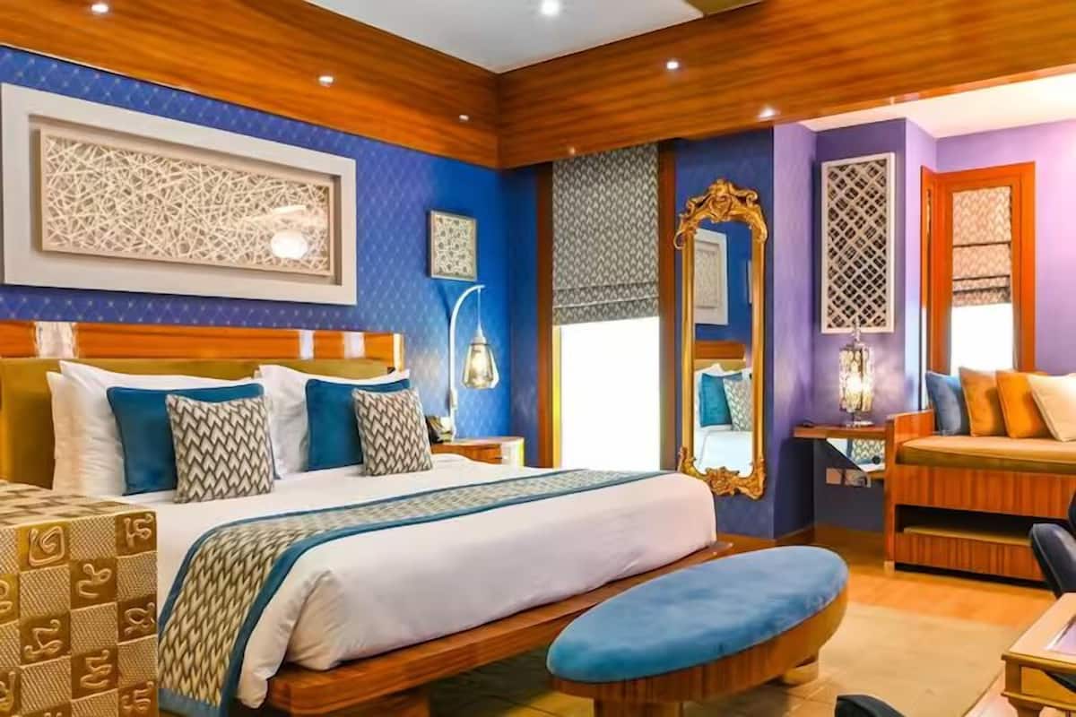 A well-lit bedroom with a large bed, bedside tables, a bench, and a mirror.