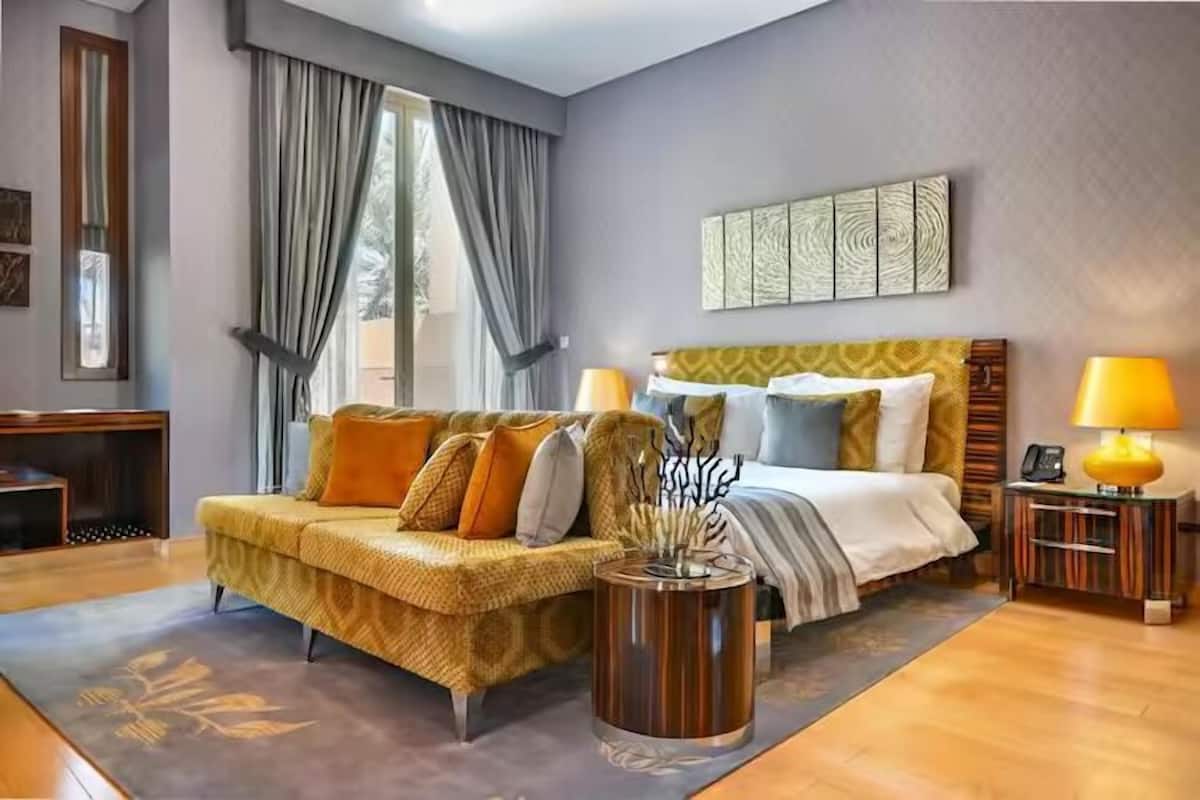 A hotel room with a bed, a sofa, a bedside table with a lamp, and a decorative vase.