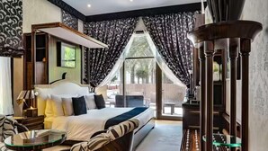 Habitación de hotel con cama, una mesita de vidrio, una silla, un ventanal con cortinas y vistas al exterior.