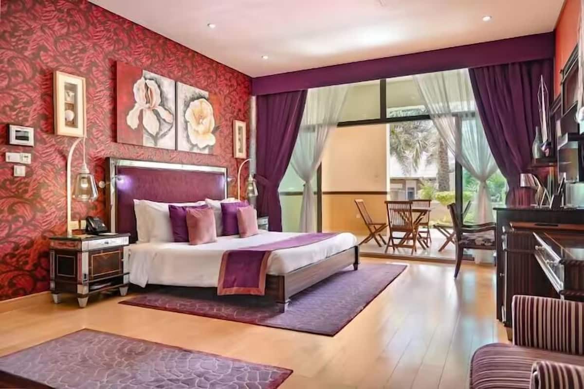 A spacious bedroom with a large bed, a nightstand, a desk, and a chair.