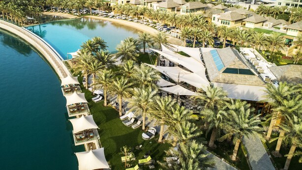 Vista aérea de un resort con una gran piscina, palmeras y villas frente a la playa.