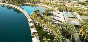 An aerial view of a resort with a large pool, palm trees, and beachside villas. - Palavra Resort (Manama)
