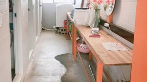A narrow hallway with a wooden bench, a table with papers, a mirror, and a hanging lamp. - Life Guesthouse - Hostel (Tongyeong)