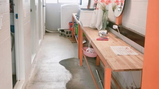 A narrow hallway with a wooden bench, a table with papers, a mirror, and a hanging lamp.