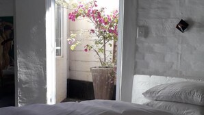 A bedroom with a bed, a potted plant, and a view of a pink flowering tree through an open door. - Alternative Space B & B (Swakopmund)