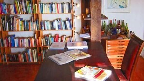 A wooden dining table with books and magazines, a wooden chair, and a bookshelf filled with books. - Alternative Space B & B (Swakopmund)