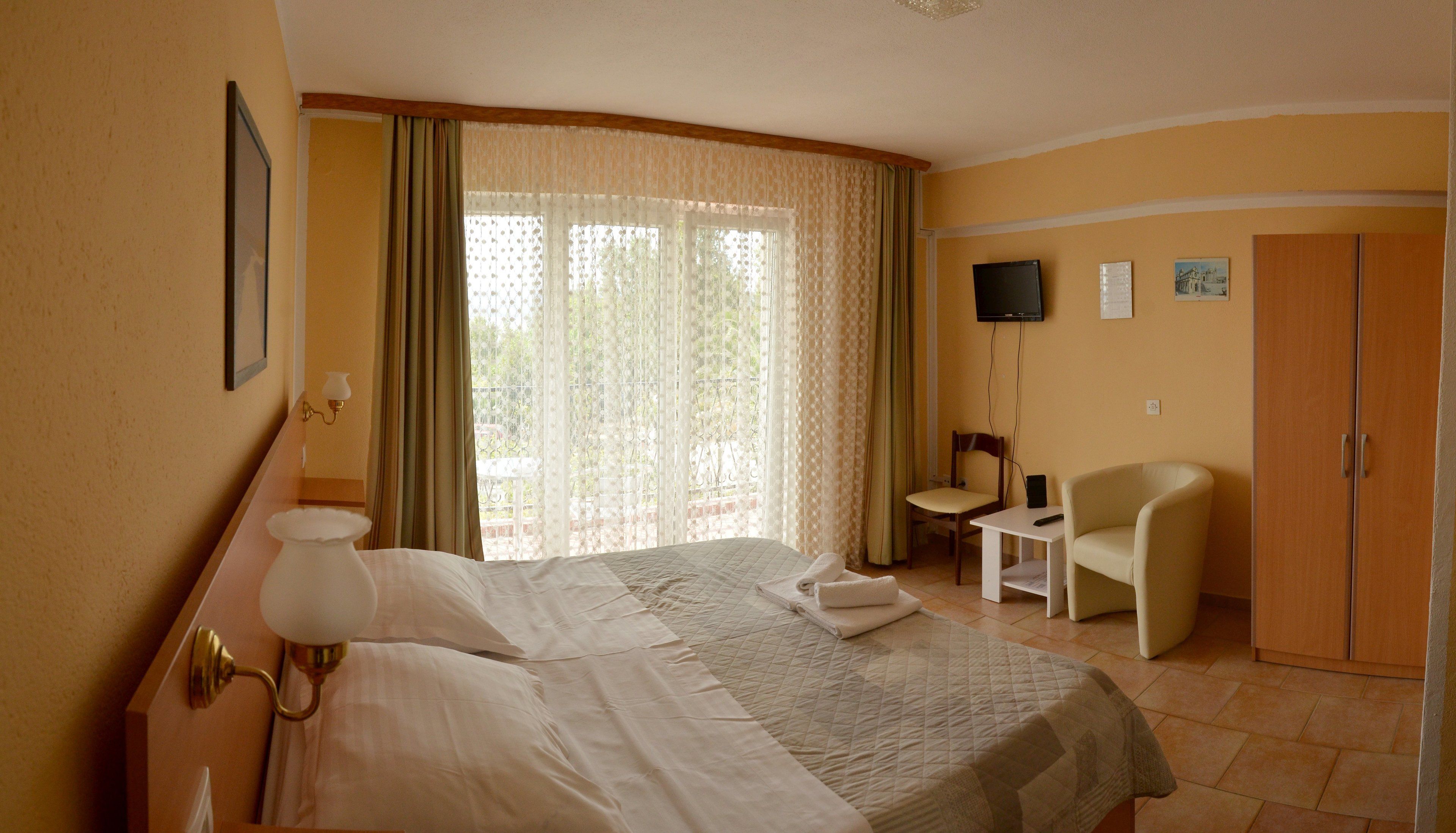 A hotel room with a bed, a desk, a chair, a TV, and a wardrobe.