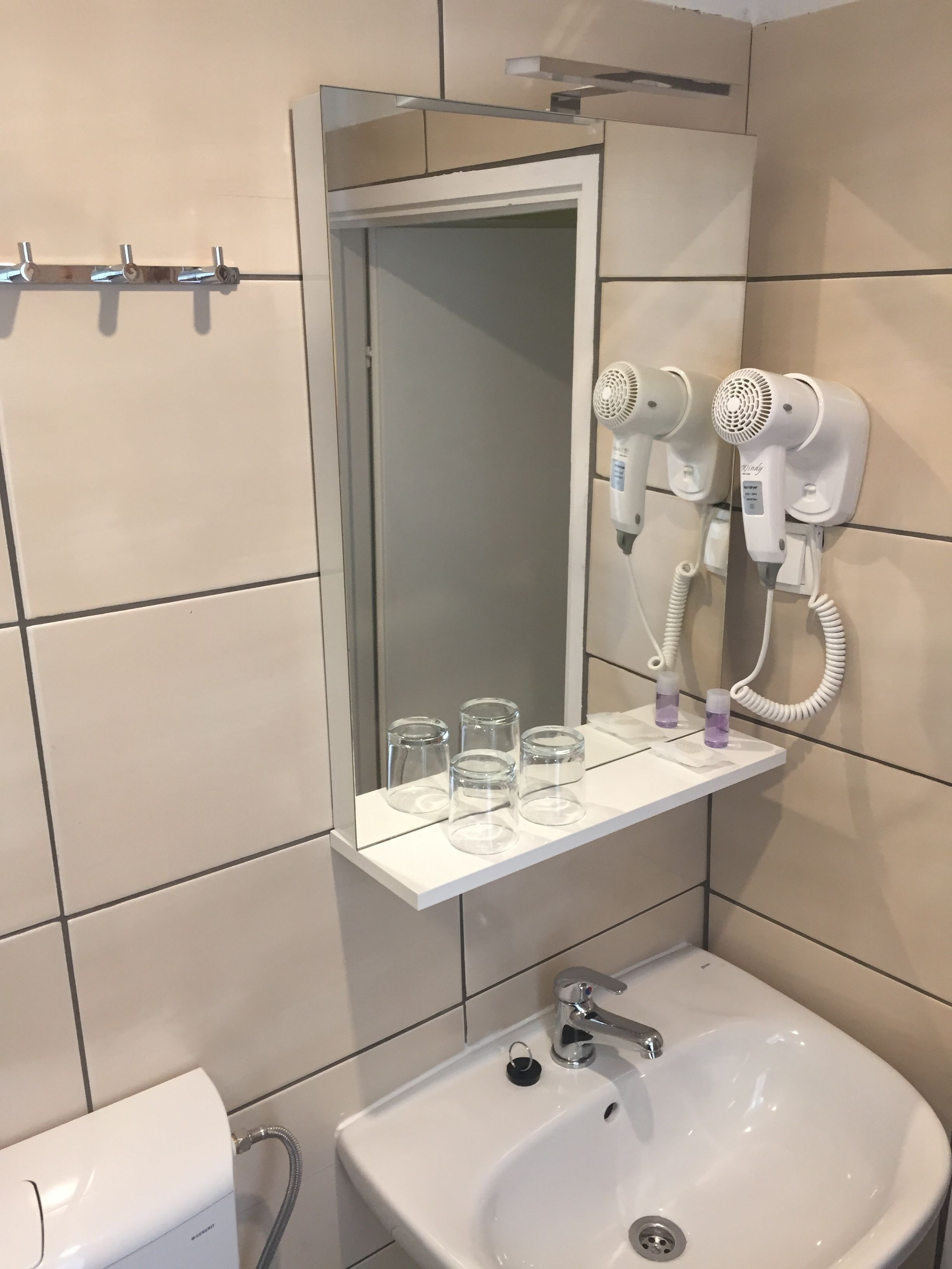 A bathroom with a sink, mirror, and two hair dryers mounted on the wall.