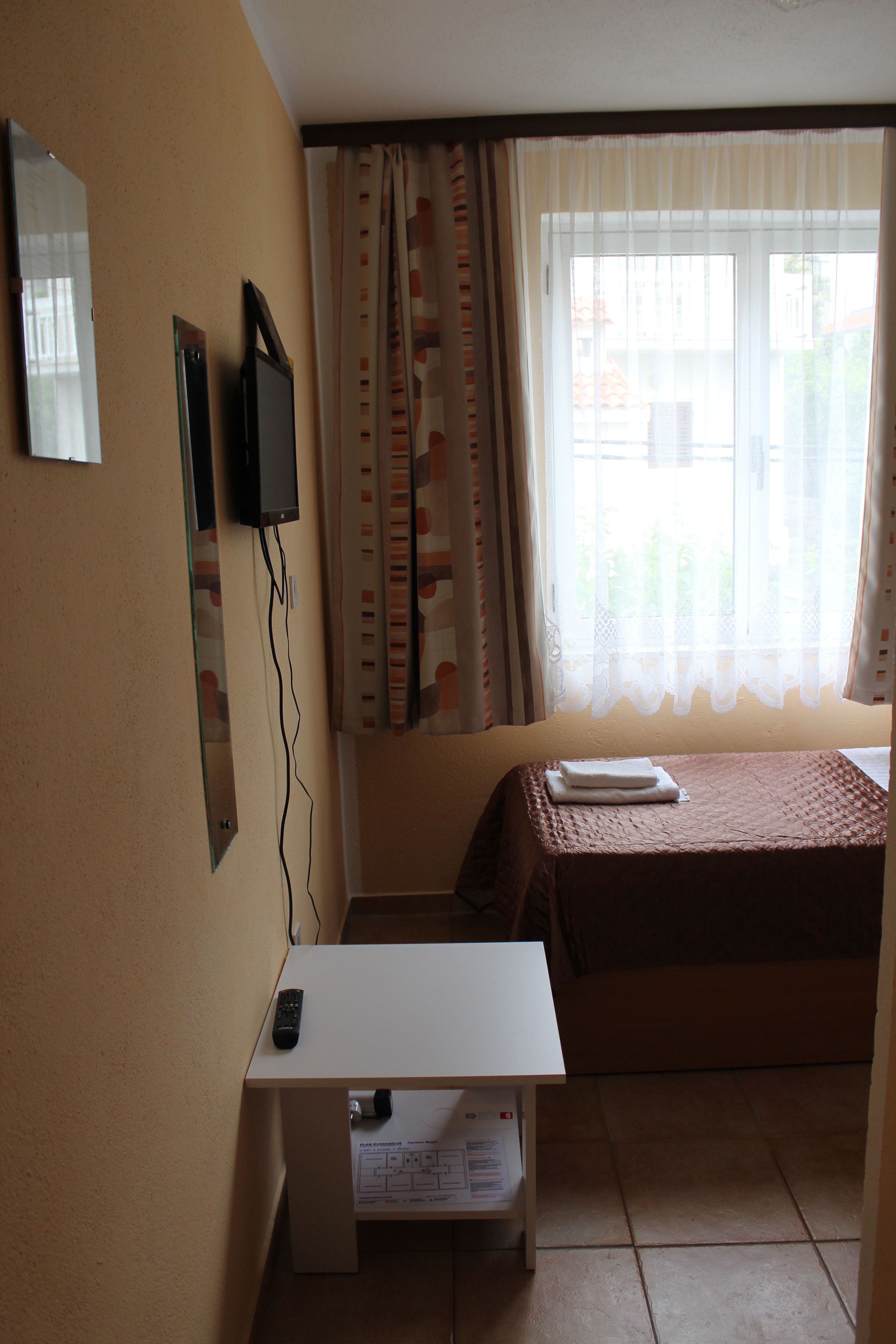 Una habitación de hotel con cama, escritorio, televisor montado en la pared y ventana con cortinas.