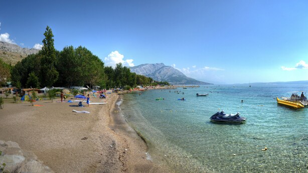 A beach with clear water, tents, and a mountainous backdrop. - Pansion Begić (Dugi Rat)