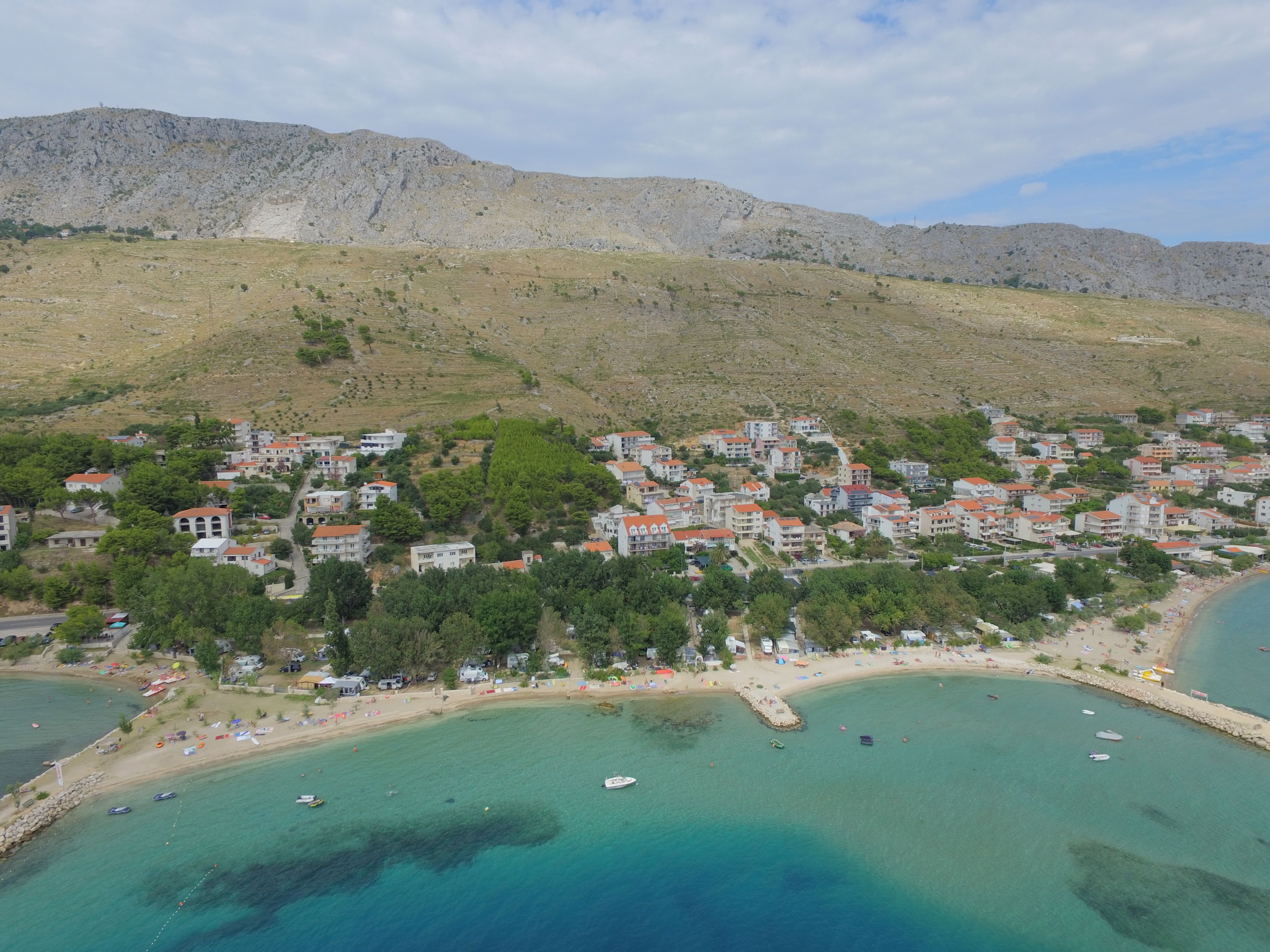 A coastal town with buildings on a hillside, a beach, and clear turquoise waters.