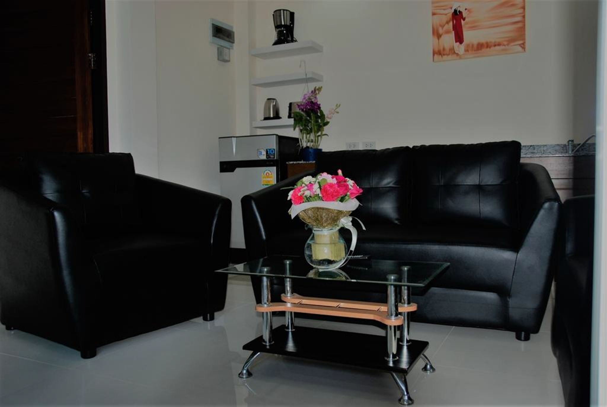 A modern living room with a black leather sofa, a glass coffee table, and a vase with flowers.