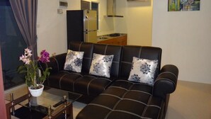 Ein Wohnzimmer mit einer schwarzen Ledersofa, zwei blumigen Kissen, einem Glastisch und einer Topfpflanze.