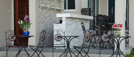 An outdoor patio with a pool, featuring a bar area with a stone wall, metal chairs, and a table with a potted plant.