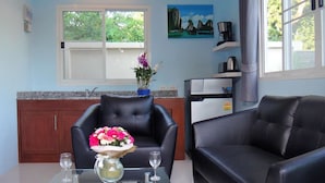 Ein Wohnzimmer mit einem Glastisch, zwei schwarzen Ledersofas, einem schwarzen Lederessel sowie einer Blumenvase und einem Bild an der Wand.