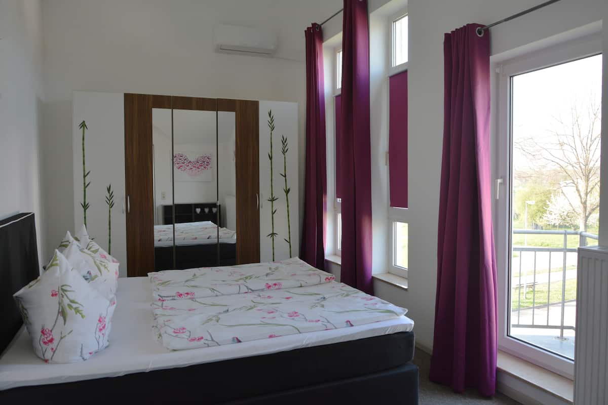 Un dormitori amb un llit, un mirall i una finestra amb cortines.