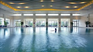 A large indoor swimming pool with a modern ceiling design, large windows, and seating areas along the sides. - Jinji Lake Grand Hotel (Suzhou)