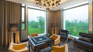 Quarto de hotel com uma grande janela, um candelabro, mesa de bilhar e um sofá.