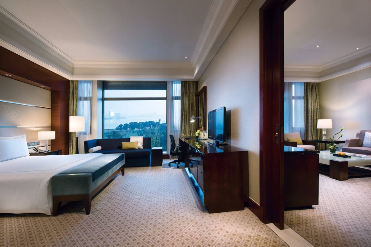 A hotel room with a large bed, a desk, a chair, a TV, and a view of the outdoors.