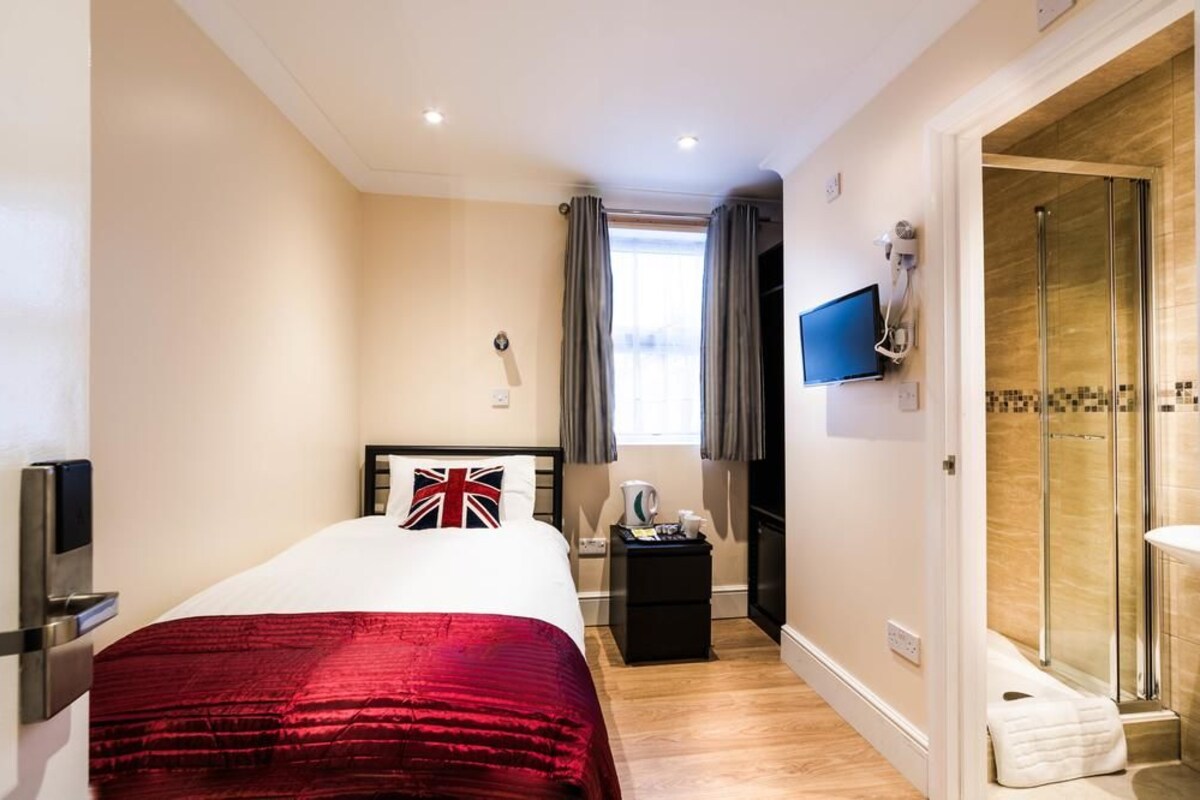 A hotel room with a bed, a television, a shower, and a window with curtains.