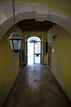 A hallway with a stone archway, a hanging lantern, and a door with a metal gate. - BB Opera dei Pupi (Syracuse)