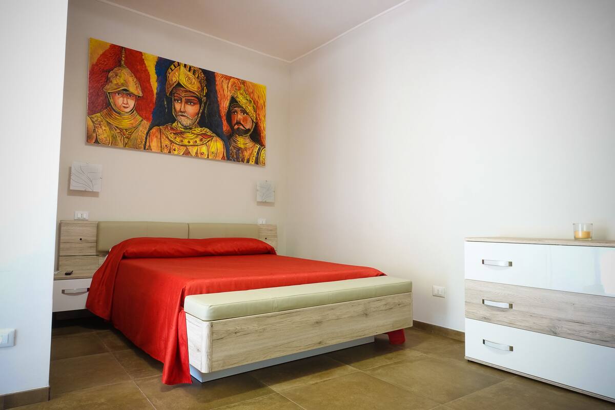 A bedroom with a bed, a dresser, and a painting on the wall.