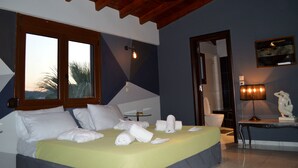 A hotel room with a bed, a desk, a lamp, a mirror, and a view of palm trees through the window. - Gold Luxury Villa Ialysos (Rhodes)