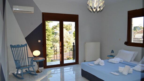 A bedroom with a bed, a rocking chair, a table with a lamp, and a view of the outdoors through a sliding door. - Gold Luxury Villa Ialysos (Rhodes)
