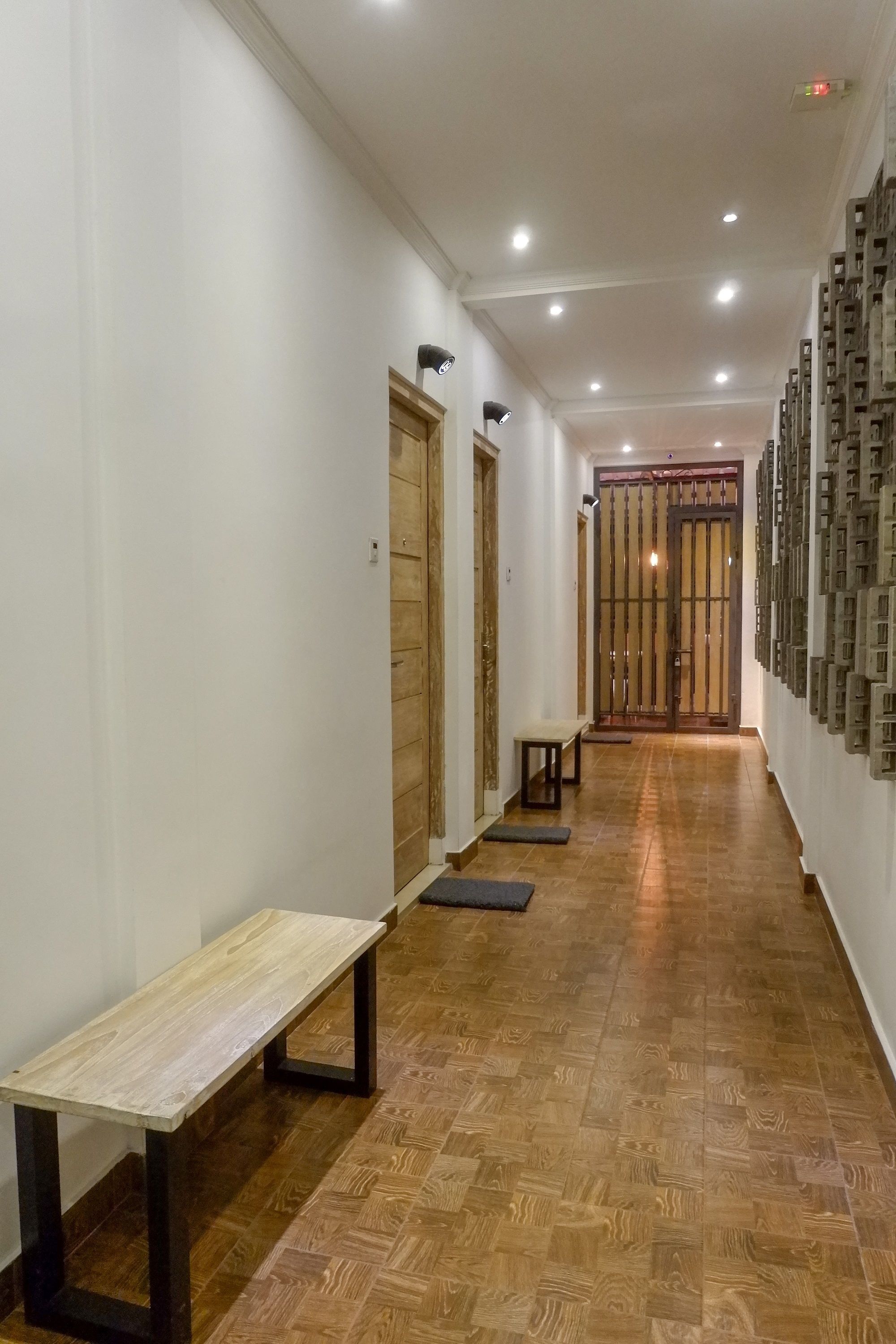 A hallway with wooden flooring, a bench, and a wall-mounted light fixture.