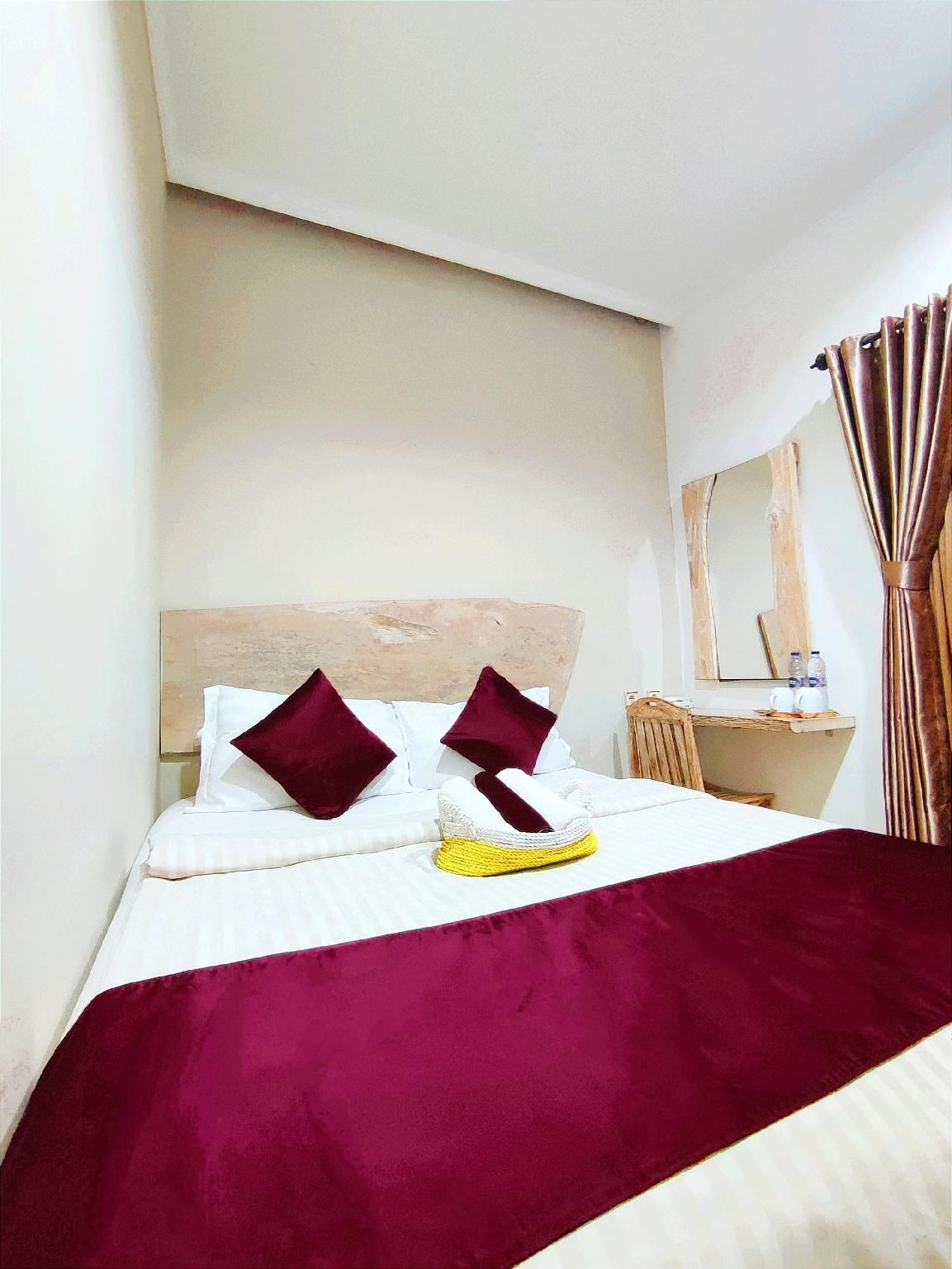 Habitación de hotel con cama, cabecera de madera, espejo, mesita con una botella y cortina.