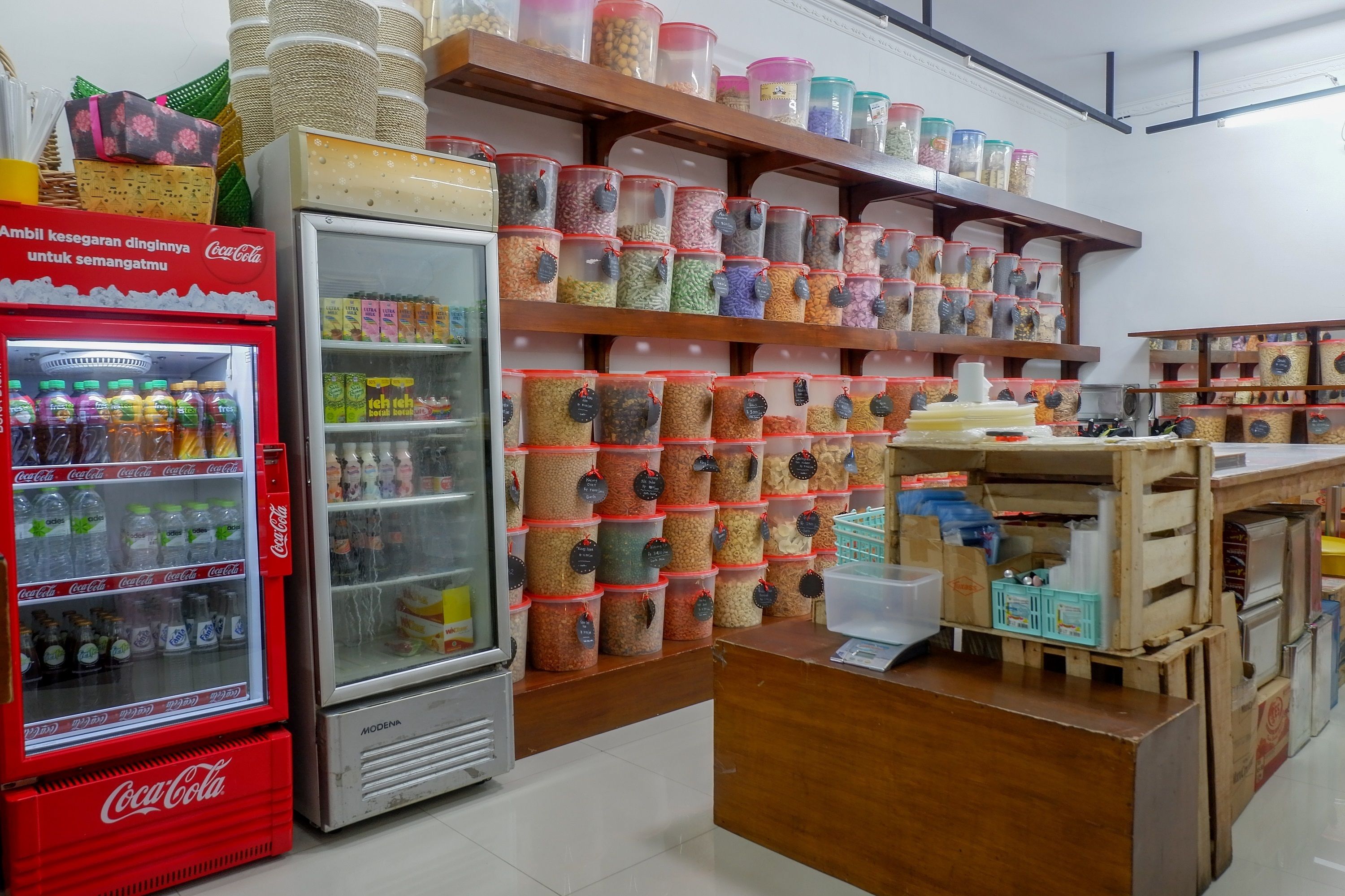 A store with shelves of colorful containers, a Coca-Cola refrigerator, and a wooden counter.