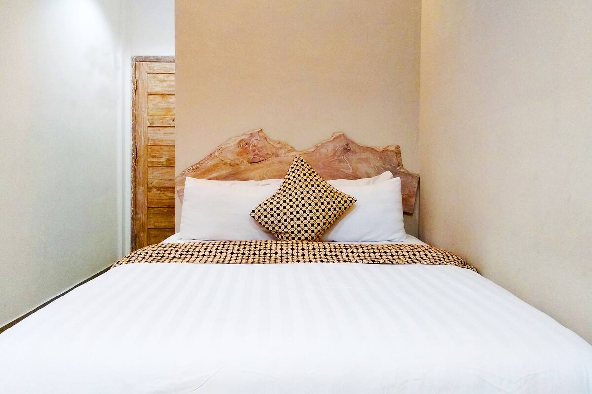 A neatly made bed with a patterned bedspread and pillows, a wooden headboard, and a stone-like wall decoration.