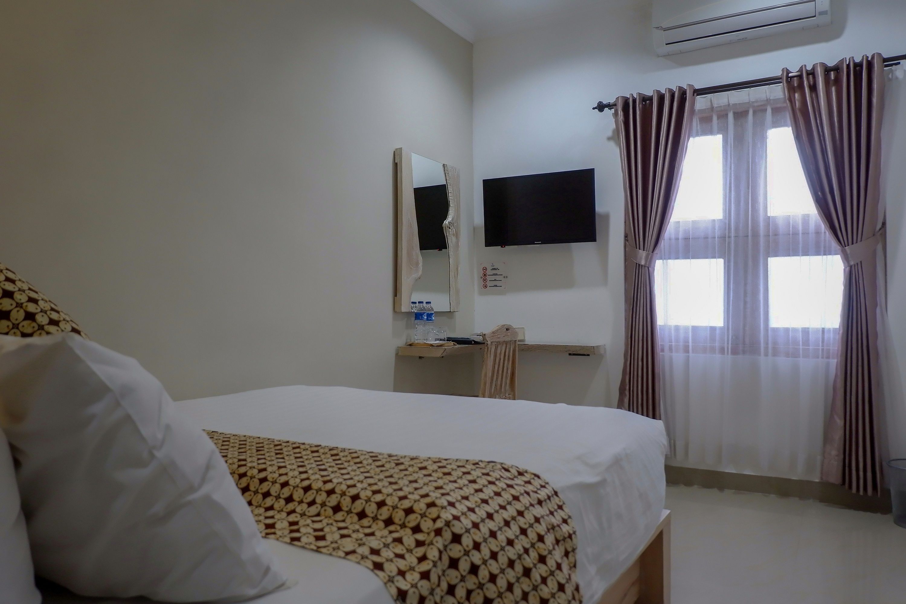 A hotel room with a bed, a desk, a flat-screen TV, and a window with curtains.