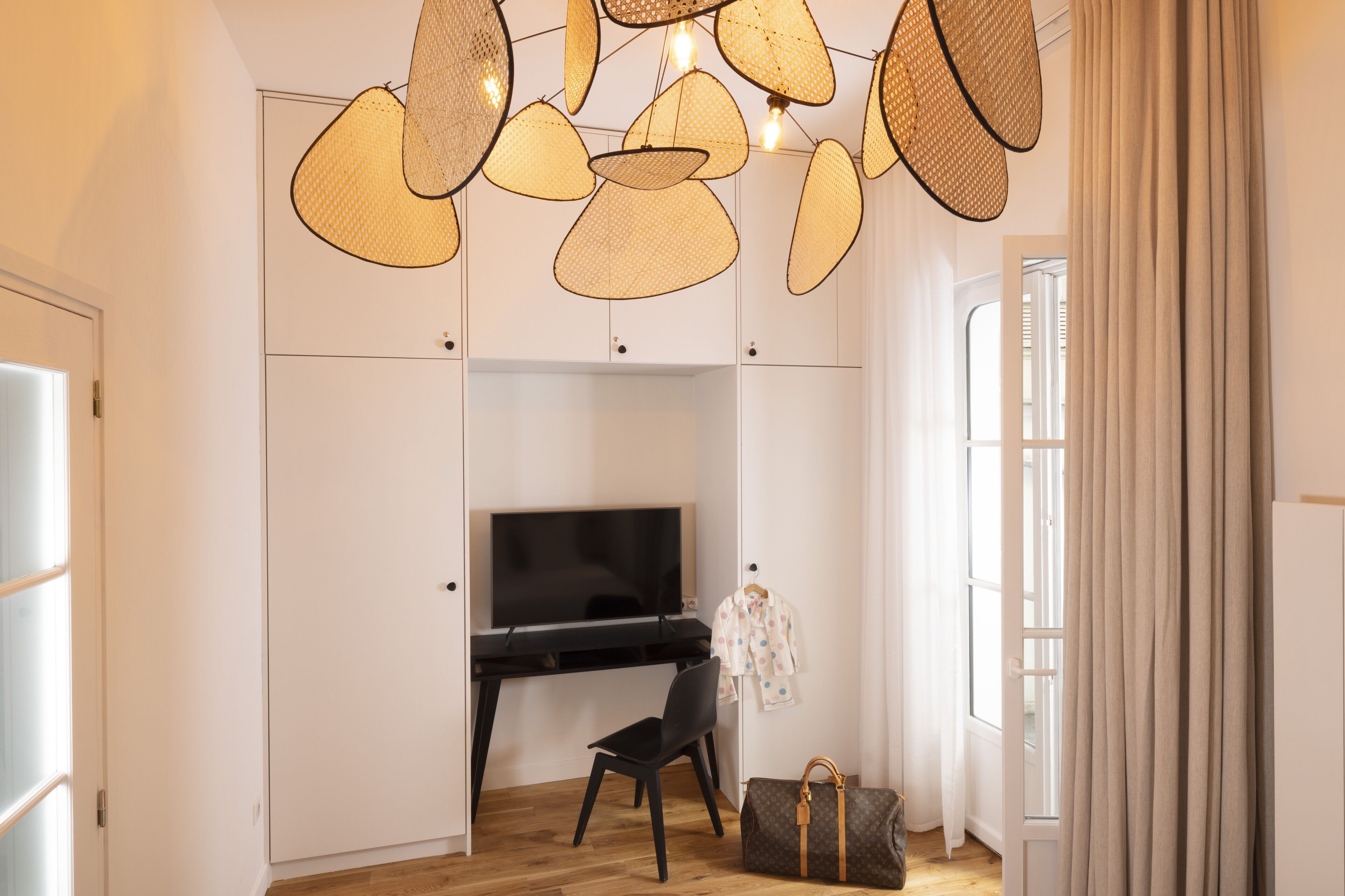 A modern room with a flat-screen TV, a black chair, a brown handbag, and a unique woven light fixture.