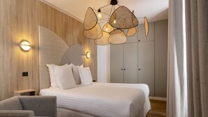 A modern bedroom with a large bed, a grey armchair, a side table with books, and a unique hanging light fixture. - Yuna Blanche - Serviced Apartments (Paris)