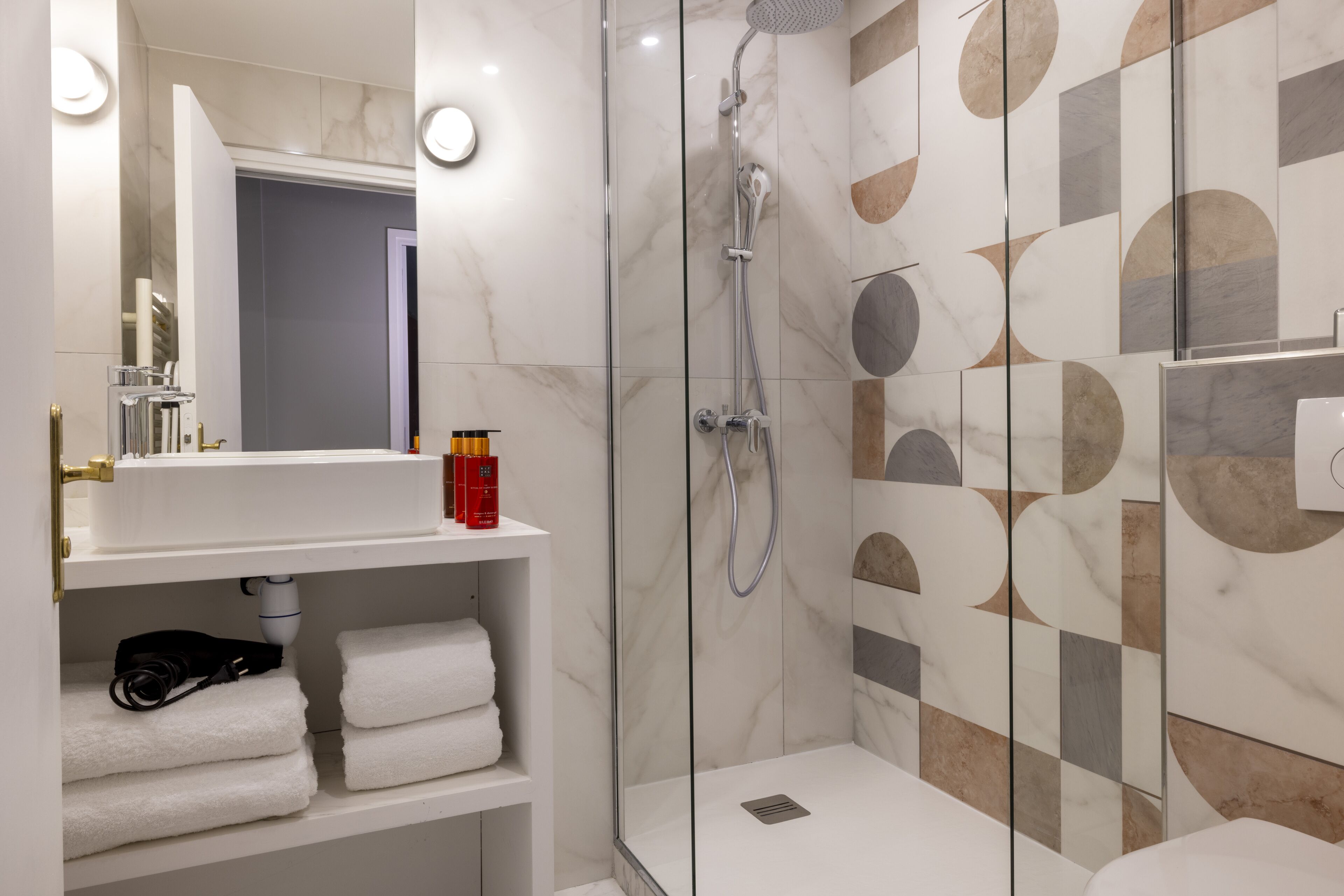 Un baño moderno con ducha envuelta en vidrio, azulejos de mármol y un tocador blanco con toallas.