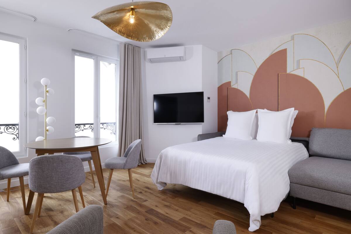 A modern hotel room with a large bed, a flat-screen TV, a dining table, and a sofa.