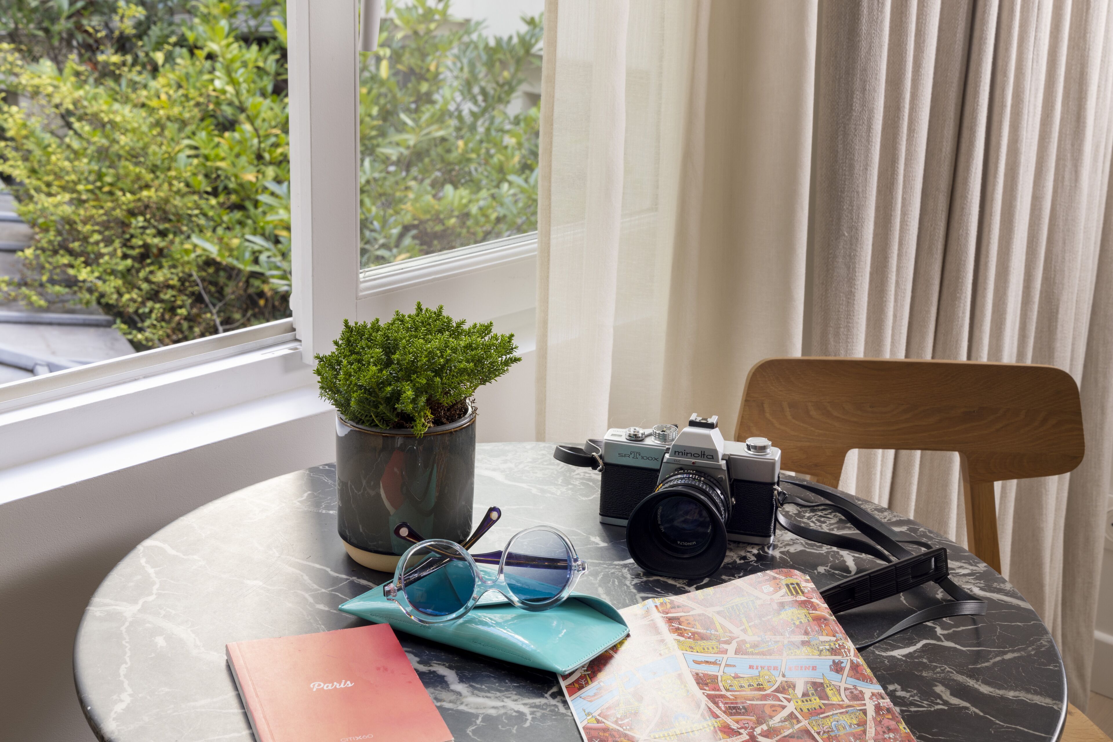 Una mesa redonda con una planta en maceta, una cámara, un par de gafas de sol, un mapa y un libro titulado 'París'.