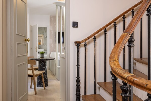 A staircase with a wooden handrail and black balusters, leading to a room with a white door and a small table with a potted plant.