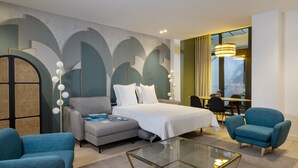 A modern hotel room with a bed, sofa, armchair, and a glass coffee table. - Yuna Blanche - Serviced Apartments (Paris)