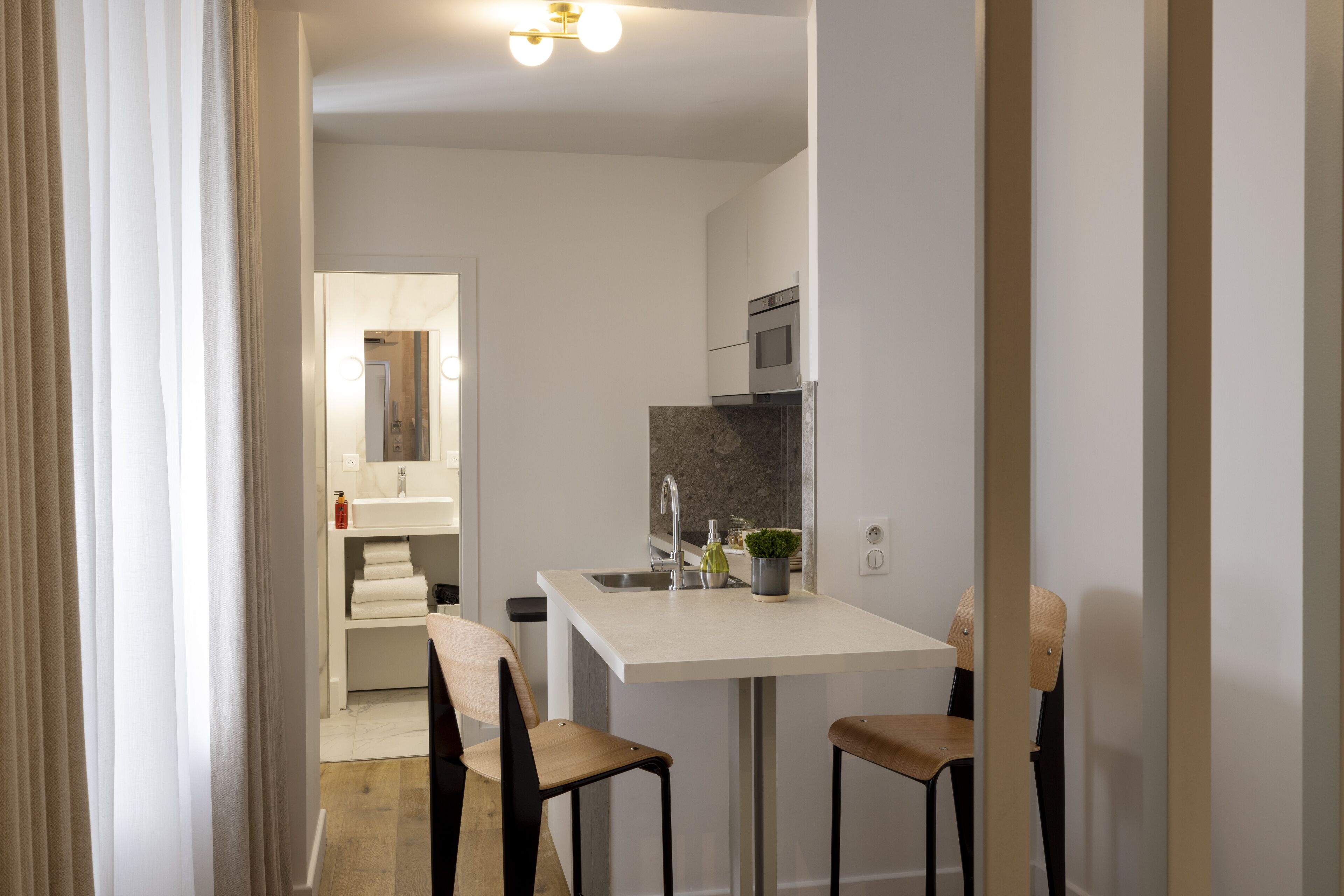A modern kitchen with a white countertop, two bar stools, a sink, and a microwave.