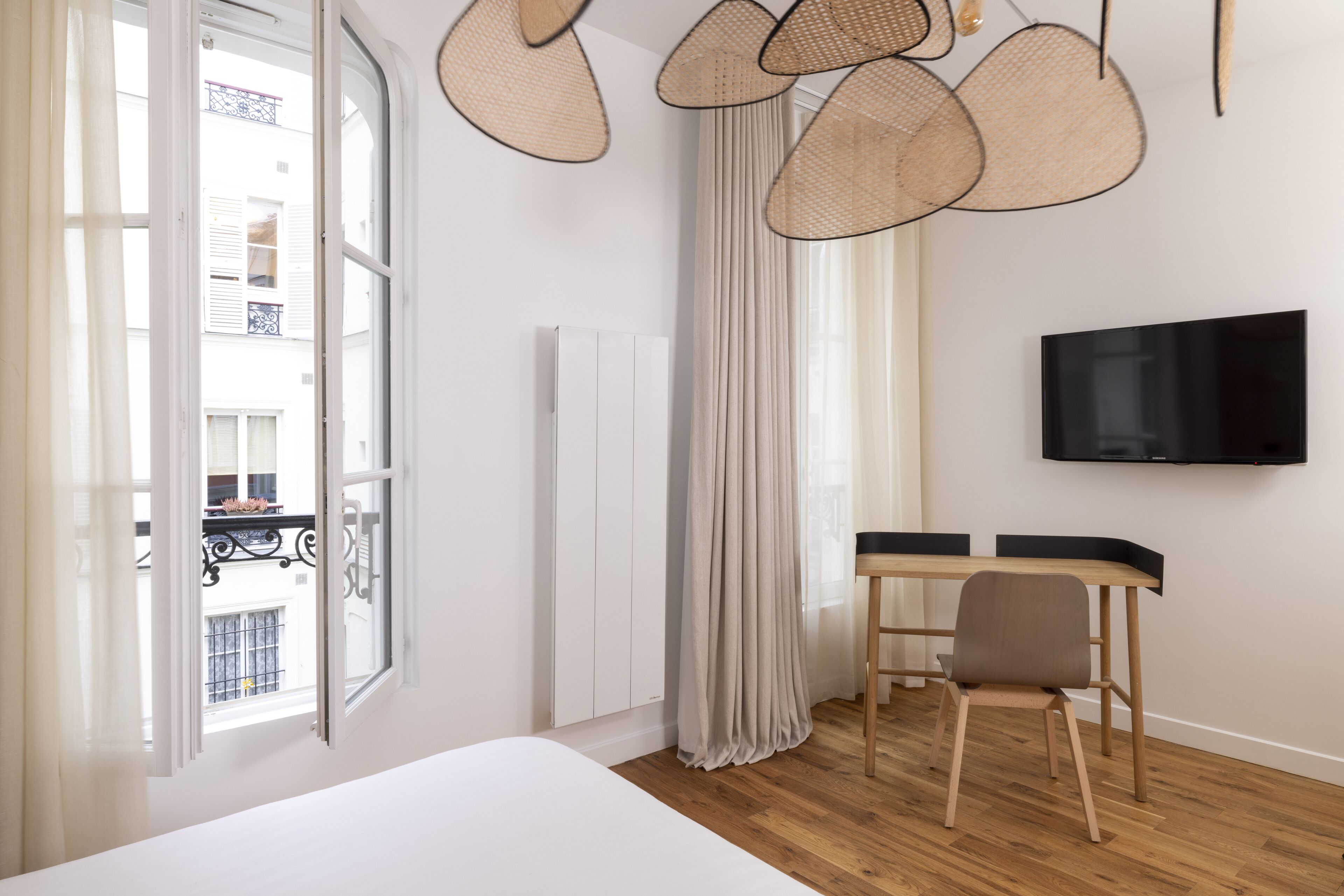 A bedroom with a bed, a desk, a chair, a TV, and a window with curtains.